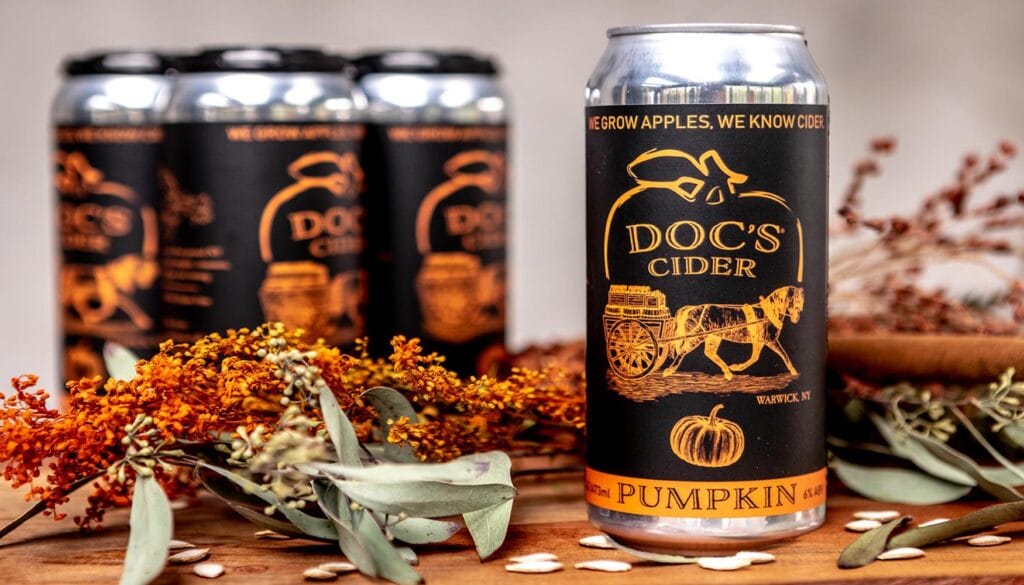 A can of Doc's Cider Pumpkin variety lying on a bed of autumn leaves, featuring vibrant red, orange, and yellow foliage.